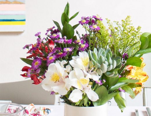 Succulent Bouquet of Cute Flowers in Purple, white, Green and Red in a White Vase on a Table Setting with a Painting in the Background