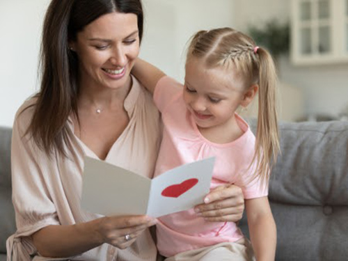 Mom reading homemade Mothers Day card with daughter.