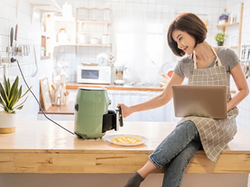 Woman in apron with a laptop using an air fryer