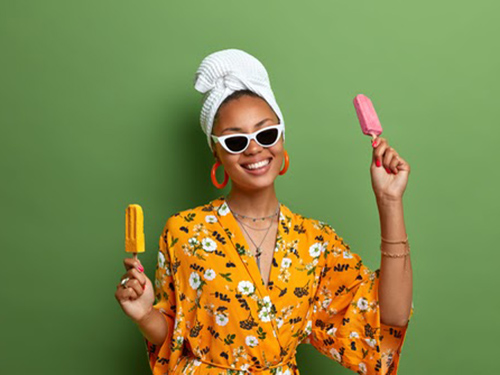 Woman in summer robe with a hair wrap holding a popsicle in each hand.