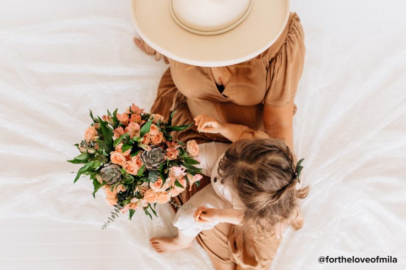 Mother with a child in her lap looking at a peach and green bouquet.