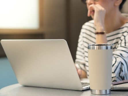 Smart looking woman with laptop and her drink in a reusable insulated tumbler mug on the table.