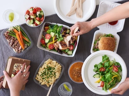 overhead spread of assorted takeout restaurant food with hands serving food