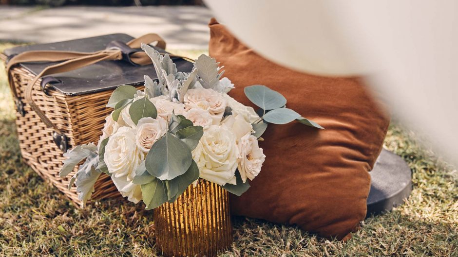 white flowers in a rustic metal vase next to picnic basket