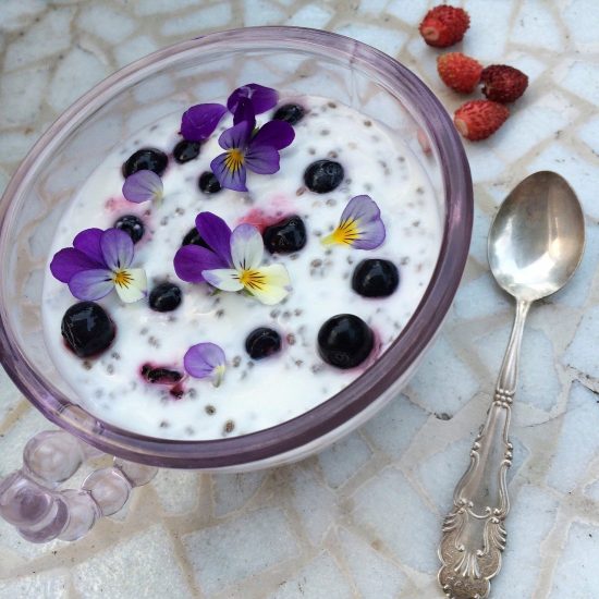 bowl containing white liquid, blueberries, and purple and white flowers