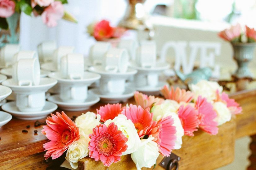 pink and white flowers on a table with white teacups and saucers