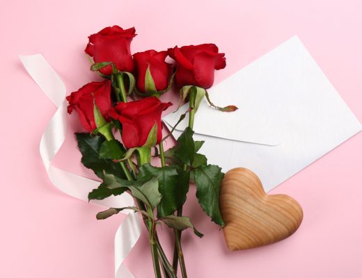 Red roses laying flat on a surface with a heart-shaped trinket and blank note.