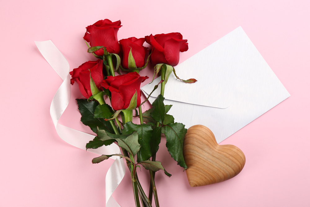 Red roses laying flat on a surface with a heart-shaped trinket and blank note.