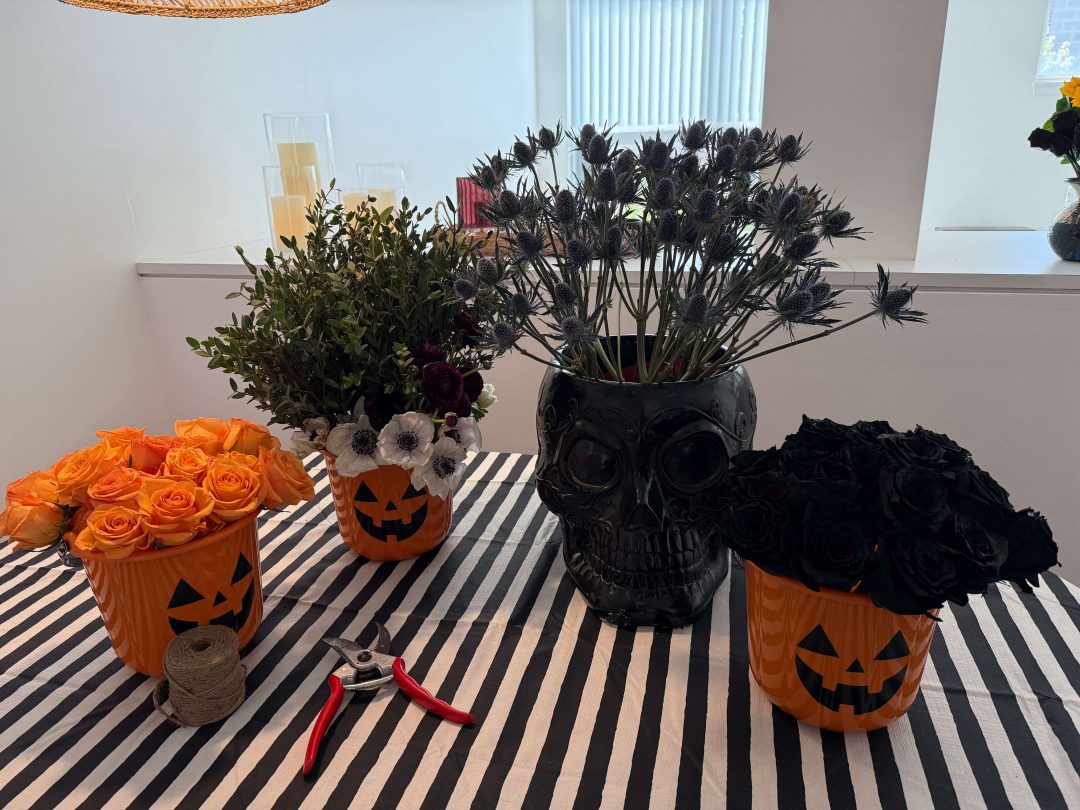 Four Halloween-themed vases of flower stems on a table with a black and white striped cover.