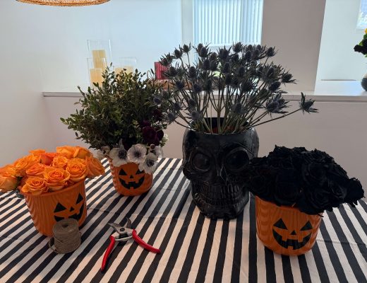 Four Halloween-themed vases of flower stems on a table with a black and white striped cover.