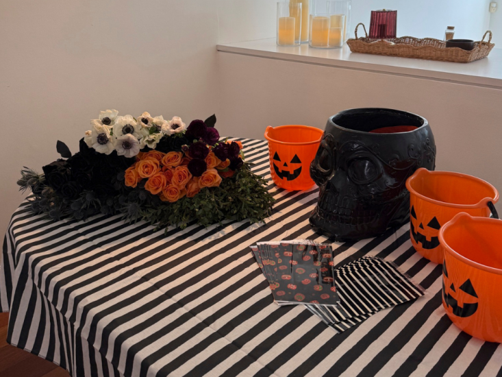 A bundle of orange, black, and white flowers displayed on a table next to Halloween-themed vases.