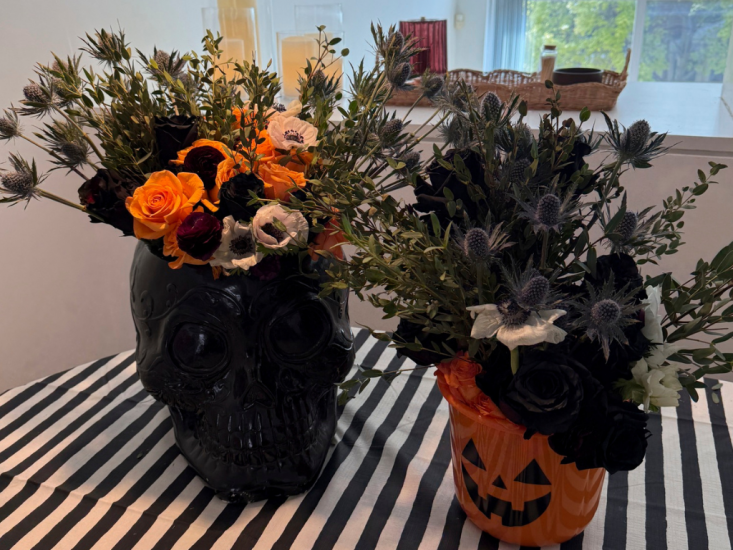 A black skull vase and jack-o-lantern pale with seasonal flowers in them.