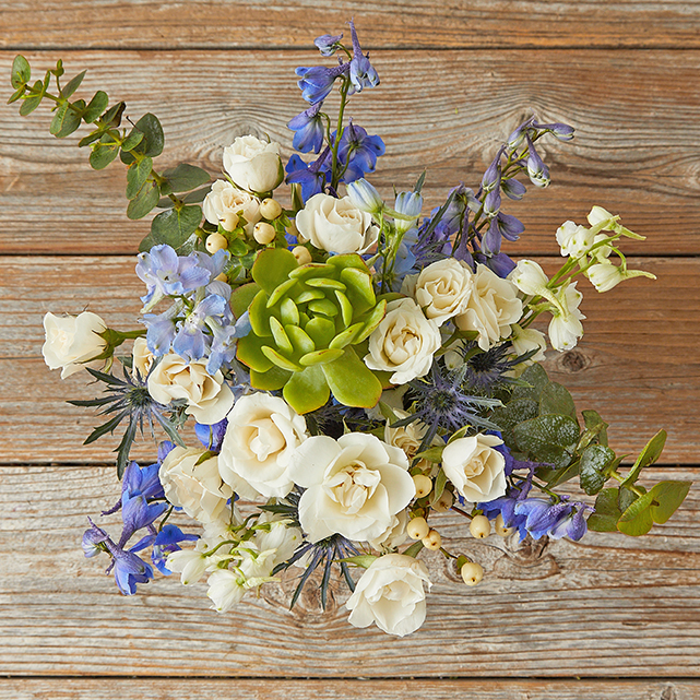 Blue delphinium and eryngium with a succulent, eucalyptus, and white spray roses.