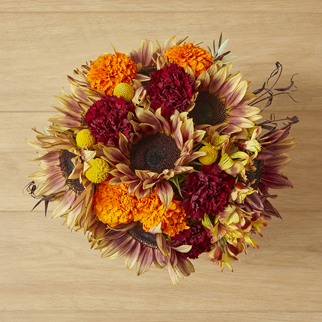 Sunflower arrangement accented by orange and red flowers including carnations and marigolds.