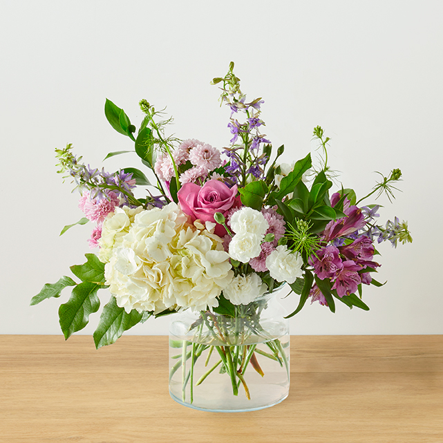 A lavender and white floral arrangement in a clear vase.