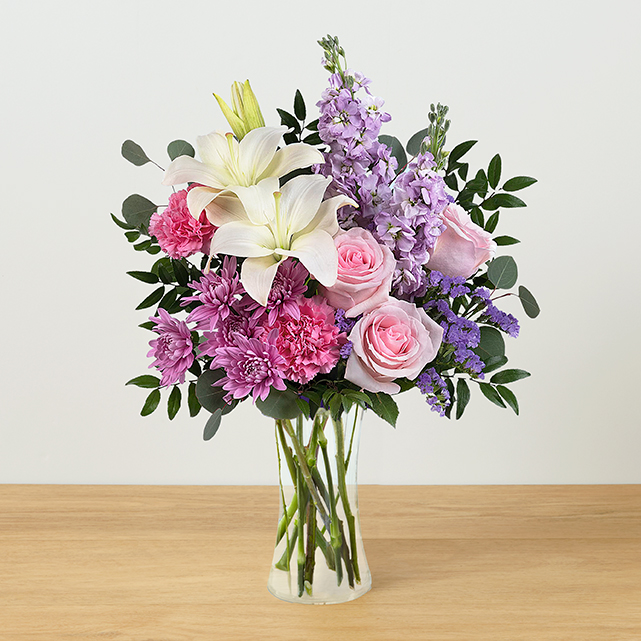 A clear vase arrangement with white lilies, pink roses, hot pink carnations and lavender stock.