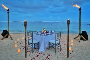 A beachside with a romantic dinner table set up with torches and rose petals surrounding it.