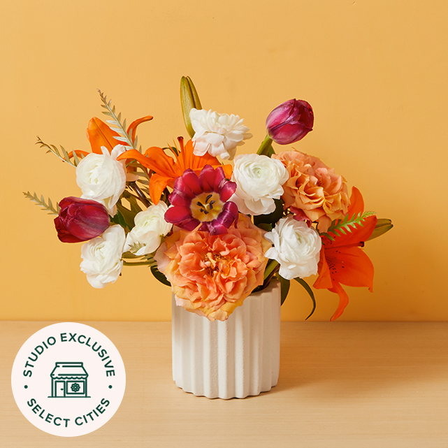 Orange and pink flowers arranged in a white vase.