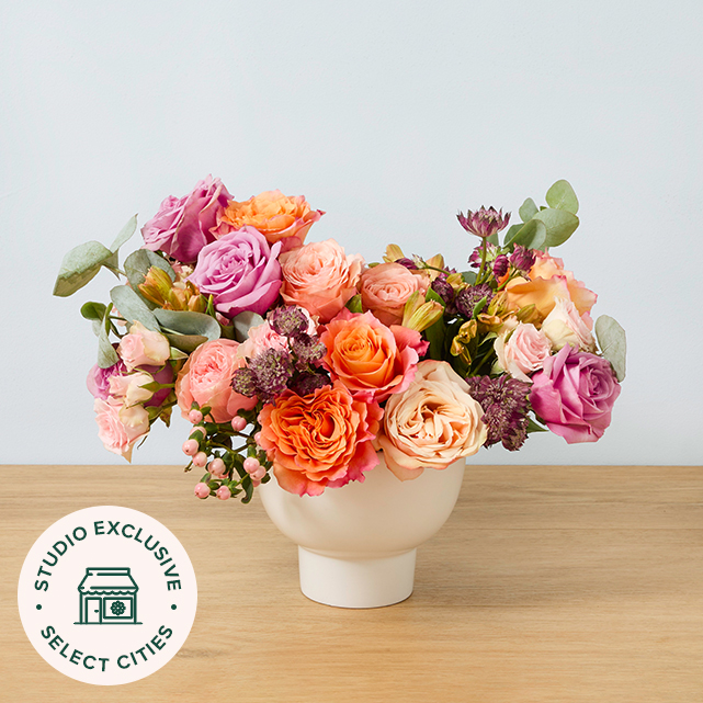 Deep colored bouquet of four different types of roses in peach, purple, orange, and pink.