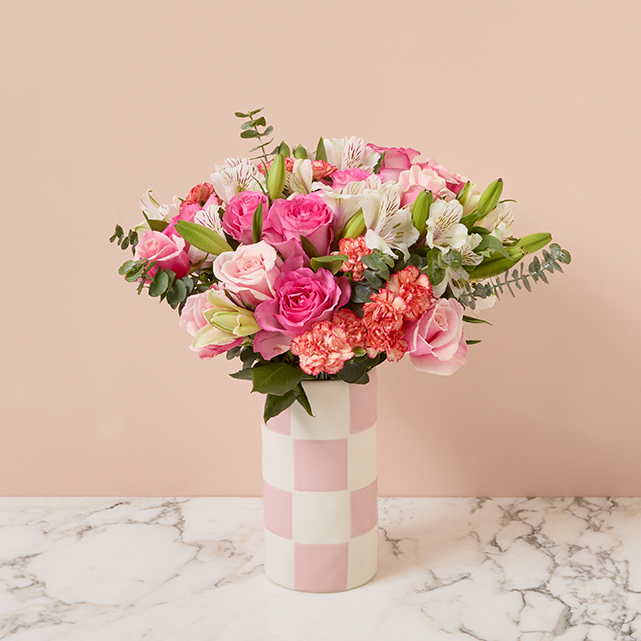 Bright pink flowers including roses and carnations in a pink checkered vase.