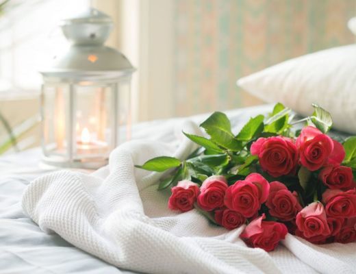 Red roses laying on a white bed with a lantern in the background.