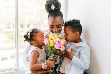 Children embracing Mom and smelling flowers.