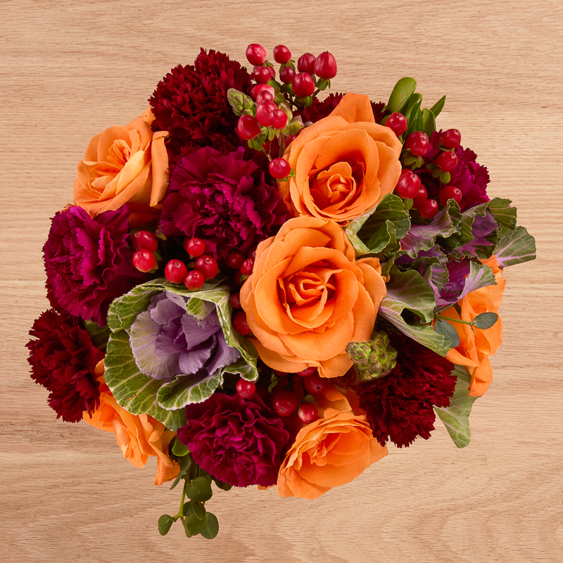 purple kale, red berries, and orange rose floral arrangement
