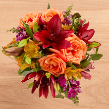 Deep colored arrangement with red lilies, burgundy snapdragons, and orange roses and alsros.