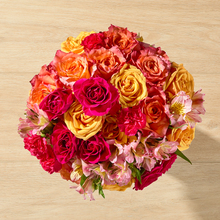 A bright-colored mix of flowers in reds, oranges, and yellows, including mixed roses, alstroemeria, and mini carnations.
