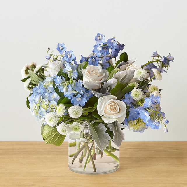 A clear vase arranged with white and sky blue flowers.