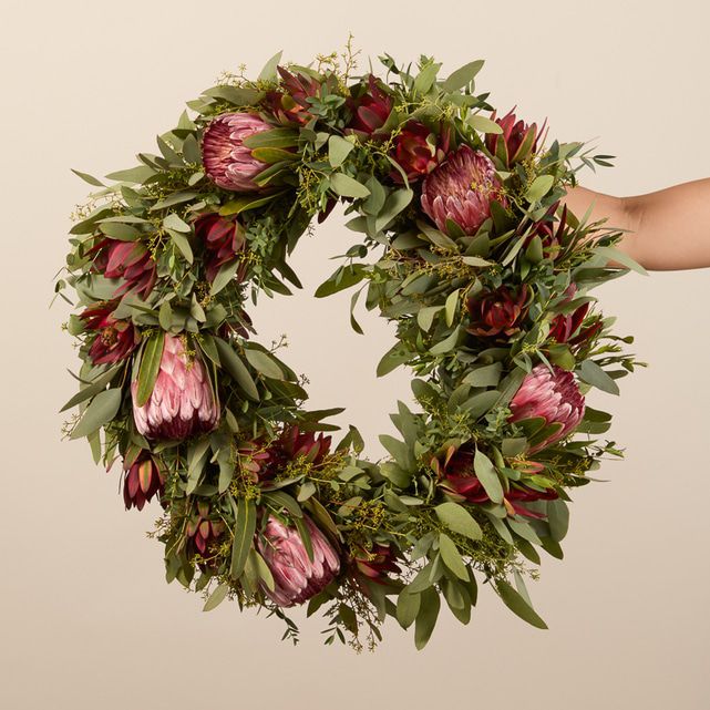 An outstretched hand holding a fresh protea wreath.