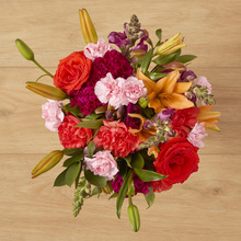 A mixed bouquet in orange, pink, and purple that features rosses, carnations, and a lily.