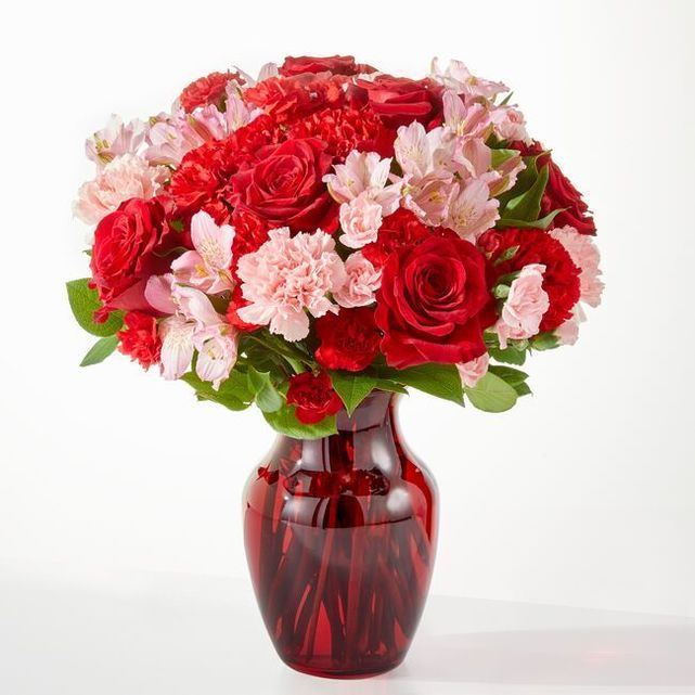 An arrangement in a red glass vase with roses and carnations.