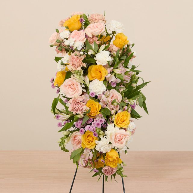 mixed floral casket spray in yellow, white, pink and other pastel colors